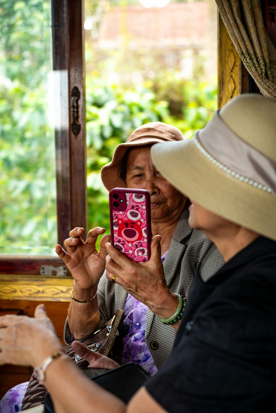 Older Asian woman in a sun hat holding up her phone
